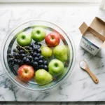 Fresh apples, pears, and grapes soaking in a baking soda water bath on a marble countertop