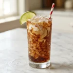 Glass of Dirty Dr Pepper with nugget ice, cream swirl, and a lime wedge